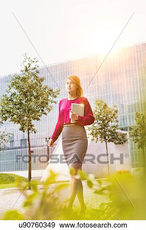 Stock Photo - Portrait of young attractive businesswoman walking while holding digital tablet . Fotosearch