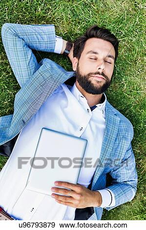 Portrait of young attractive businessman holding digital tablet while sleeping and lying on the grass View Large Photo Image Stock Photo - Portrait of young attractive businessman holding digital tablet while sleeping and lying on the grass. Fotosearch