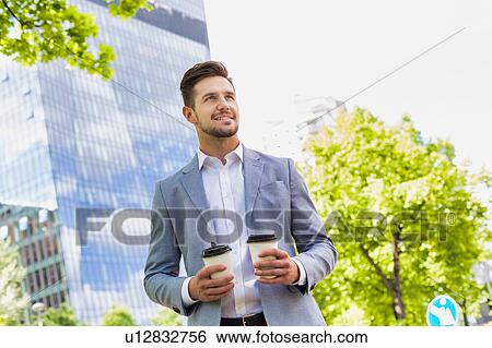 Stock Photograph - Portrait of young attractive businessman holding two cups of coffee . Fotosearch