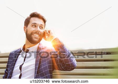 Stock Photograph - Portrait of young attractive businessman smiling while talking on smartphone. Fotosearch