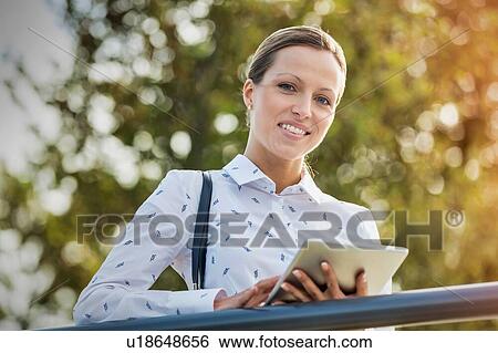 Stock Photograph - Portrait of young attractive businesswoman using digital tablet while leaning on railing. Fotosearch