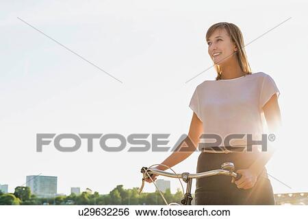 Stock Photograph - Portrait of young attractive businesswoman holding bicycle while walking on the beach . Fotosearch