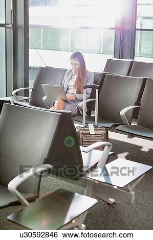 Stock Photograph - Portrait of young attractive businesswoman sitting and working with her laptop while waiting for boarding at airport. Fotosearch