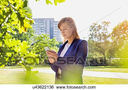 Stock Photograph - Portrait of young attractive businesswoman using smartphone in park. Fotosearch