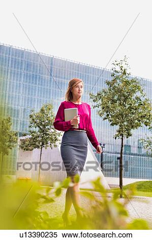 Stock Photography - Portrait of young attractive businesswoman walking while holding digital tablet . Fotosearch
