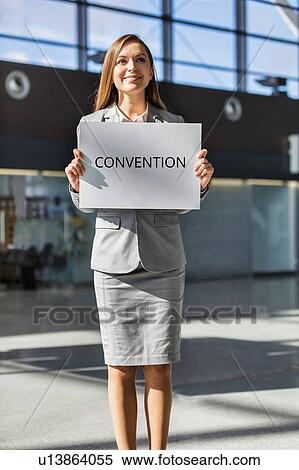 Portrait of young attractive businesswoman standing while holding white board with CONVENTION signage in arrival area at airport View Large Photo Image Stock Photography - Portrait of young attractive businesswoman standing while holding white board with CONVENTION signage in arrival area at airport. Fotosearch