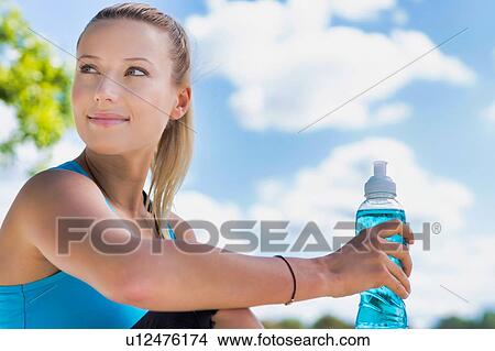 Picture - Portrait of young attractive woman drinking energy drink in park. Fotosearch