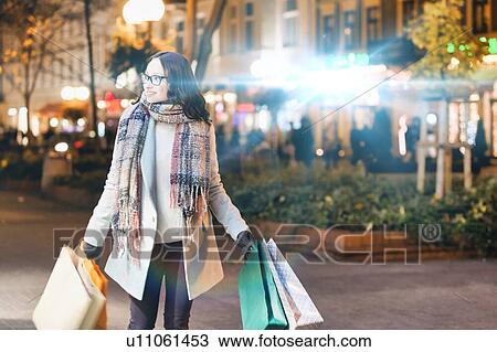 Portrait of young attractive woman walking while holding paper bags on night shopping View Large Photo Image Stock Image - Portrait of young attractive woman walking while holding paper bags on night shopping. Fotosearch
