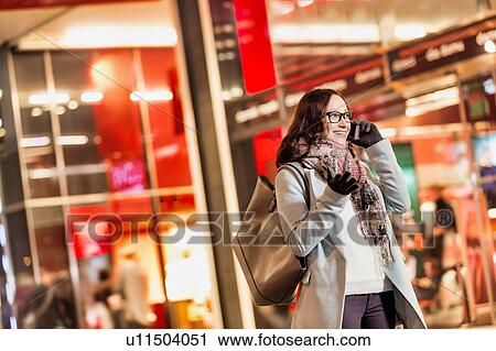 Stock Image - Portrait of young attractive woman talking on smartphone at night shopping. Fotosearch