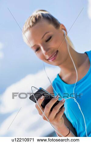 Portrait of young attractive woman standing while using and listening to music on her smartphone in park View Large Photo Image Stock Image - Portrait of young attractive woman standing while using and listening to music on her smartphone in park. Fotosearch