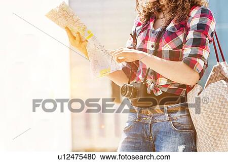 Stock Image - Portrait of young attractive woman looking on the map in the city with lens flare in background. Fotosearch