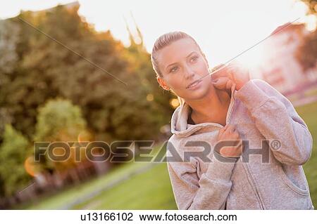 Portrait of young attractive woman smiling while standing and zipping her jacket in park View Large Photo Image Stock Image - Portrait of young attractive woman smiling while standing and zipping her jacket in park. Fotosearch