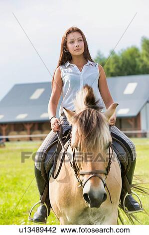 Stock Image - Portrait of young attractive woman riding horse in ranch. Fotosearch