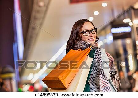 Portrait of young attractive woman walking while holding paper bags on night shopping View Large Photo Image Stock Image - Portrait of young attractive woman walking while holding paper bags on night shopping. Fotosearch