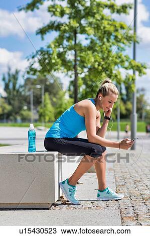 Portrait of young attractive woman sitting while using and listening to music on her smartphone in park View Large Photo Image Stock Image - Portrait of young attractive woman sitting while using and listening to music on her smartphone in park. Fotosearch