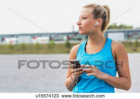 Portrait of young attractive woman standing while using and listening to music on her smartphone in park View Large Photo Image Stock Image - Portrait of young attractive woman standing while using and listening to music on her smartphone in park. Fotosearch