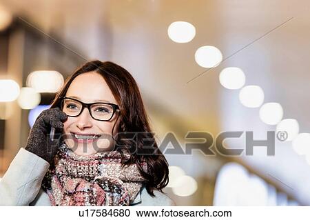 Stock Image - Portrait of young attractive woman talking on smartphone at night shopping. Fotosearch