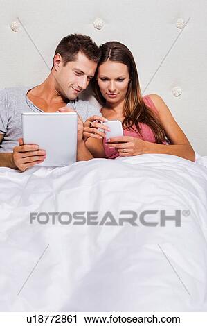 Portrait of young attractive woman showing smartphone while his boyfriend playing games on his digital tablet in bed View Large Photo Image Stock Image - Portrait of young attractive woman showing smartphone while his boyfriend playing games on his digital tablet in bed. Fotosearch
