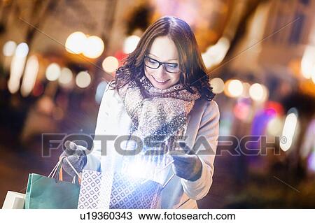 Stock Image - Portrait of young attractive woman smiling while looking at her new clothes on paper bag . Fotosearch