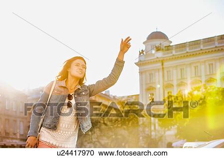 Portrait of young attractive woman calling taxi in the middle of the city with lens flare in background View Large Photo Image Stock Image - Portrait of young attractive woman calling taxi in the middle of the city with lens flare in background. Fotosearch