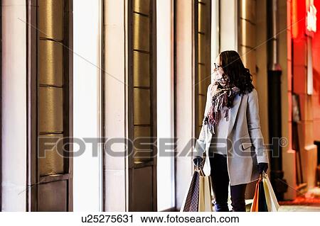 Stock Image - Portrait of young attractive woman looking at the dress on a manequin in shop through the window. Fotosearch