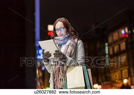 Portrait of young attractive woman smiling and using digital tablet while on night shopping View Large Photo Image Stock Image - Portrait of young attractive woman smiling and using digital tablet while on night shopping. Fotosearch