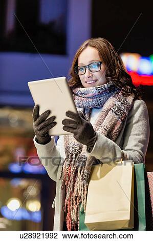 Portrait of young attractive woman smiling and using digital tablet while on night shopping View Large Photo Image Stock Image - Portrait of young attractive woman smiling and using digital tablet while on night shopping. Fotosearch
