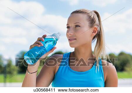 Stock Image - Portrait of young attractive woman drinking energy drink in park. Fotosearch