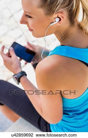 Portrait of young attractive woman sitting while using and listening to music on her smartphone in park View Large Photo Image Stock Image - Portrait of young attractive woman sitting while using and listening to music on her smartphone in park. Fotosearch