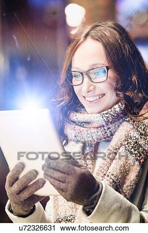 Stock Image - Portrait of young attractive woman smiling and using digital tablet while on night shopping. Fotosearch
