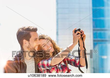 Portrait of young attractive woman taking selfie with her boyfriend in the middle of the city with lens flare in background View Large Photo Image Stock Photo - Portrait of young attractive woman taking selfie with her boyfriend in the middle of the city with lens flare in background. Fotosearch
