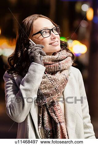 Stock Photo - Portrait of young attractive woman talking on smartphone at night shopping. Fotosearch