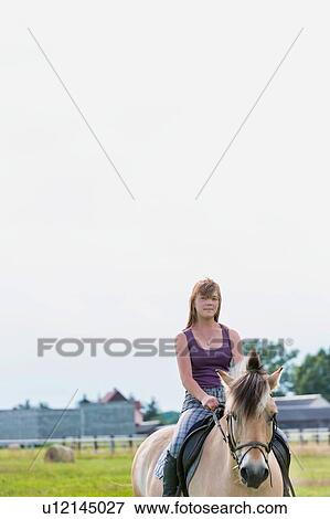 Stock Photo - Portrait of young attractive woman riding horse in ranch. Fotosearch