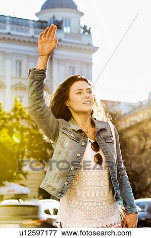Stock Photo - Portrait of young attractive woman calling taxi in the middle of the city with lens flare in background. Fotosearch