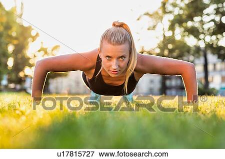 Stock Photo - Portrait of young attractive woman planking in park with lens flare. Fotosearch