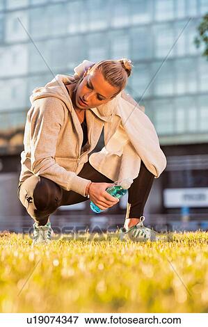 Stock Photo - Portrait of young attractive woman wiping sweat with towel in park. Fotosearch