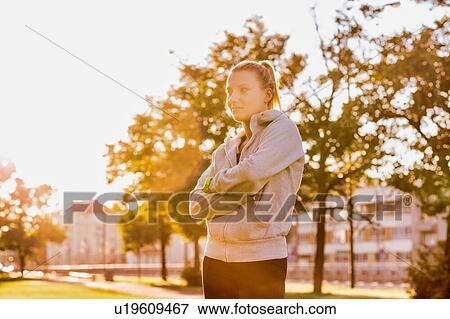 Stock Photo - Portrait of young attractive woman standing with arms crossed in park. Fotosearch