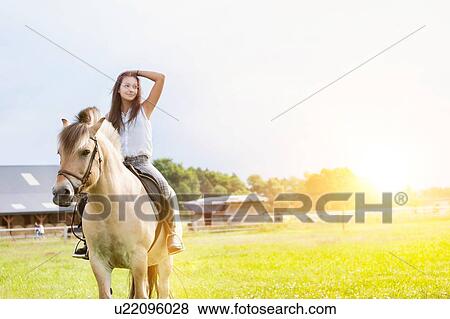 Stock Photo - Portrait of young attractive woman riding horse in ranch. Fotosearch