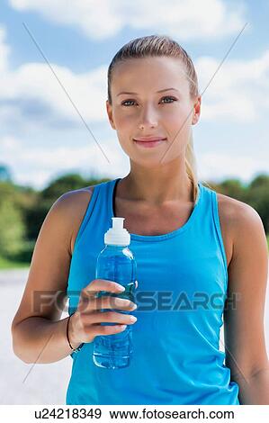 Stock Photo - Portrait of young attractive woman drinking energy drink in park. Fotosearch