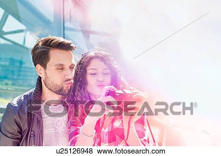 Stock Photo - Portrait of young attractive woman taking selfie with her boyfriend in the middle of the city with lens flare in background. Fotosearch