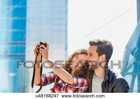 Stock Photo - Portrait of young attractive woman taking selfie with her boyfriend in the middle of the city. Fotosearch