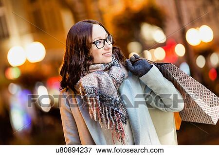 Portrait of young attractive woman walking while holding paper bags on night shopping View Large Photo Image Stock Photo - Portrait of young attractive woman walking while holding paper bags on night shopping. Fotosearch