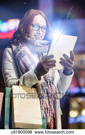 Portrait of young attractive woman smiling and using digital tablet while on night shopping View Large Photo Image Stock Photo - Portrait of young attractive woman smiling and using digital tablet while on night shopping. Fotosearch