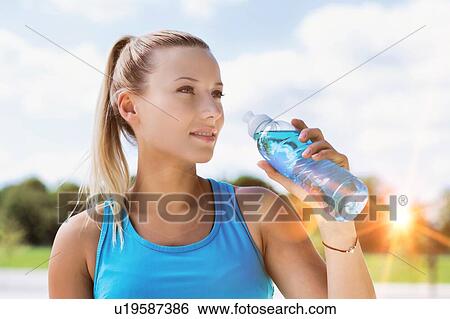 Stock Photograph - Portrait of young attractive woman drinking energy drink in park. Fotosearch