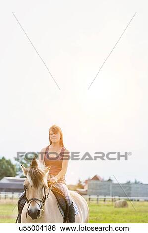 Stock Photograph - Portrait of young attractive woman riding horse in ranch. Fotosearch