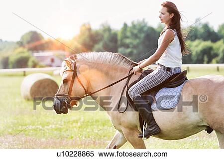 Stock Photography - Portrait of young attractive woman riding horse in ranch. Fotosearch
