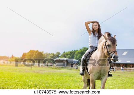 Stock Photography - Portrait of young attractive woman riding horse in ranch. Fotosearch
