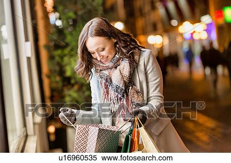 Portrait of young attractive woman smiling while looking at her new clothes on paper bag View Large Photo Image Stock Photography - Portrait of young attractive woman smiling while looking at her new clothes on paper bag . Fotosearch