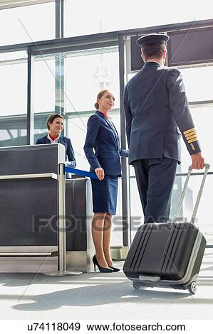 Stock Photo - Portrait of young beautiful airport staff opening the gate for boarding while mature pilot walking in airport . Fotosearch