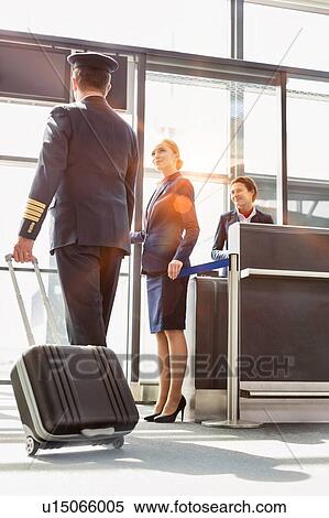 Portrait of young beautiful airport staff opening the gate for boarding while mature pilot walking in airport View Large Photo Image Stock Photography - Portrait of young beautiful airport staff opening the gate for boarding while mature pilot walking in airport . Fotosearch
